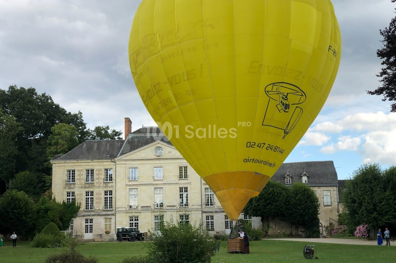 Montgolfière jaune en préparation pour un vol, posée sur une pelouse devant un manoir ancien entouré de verdure.