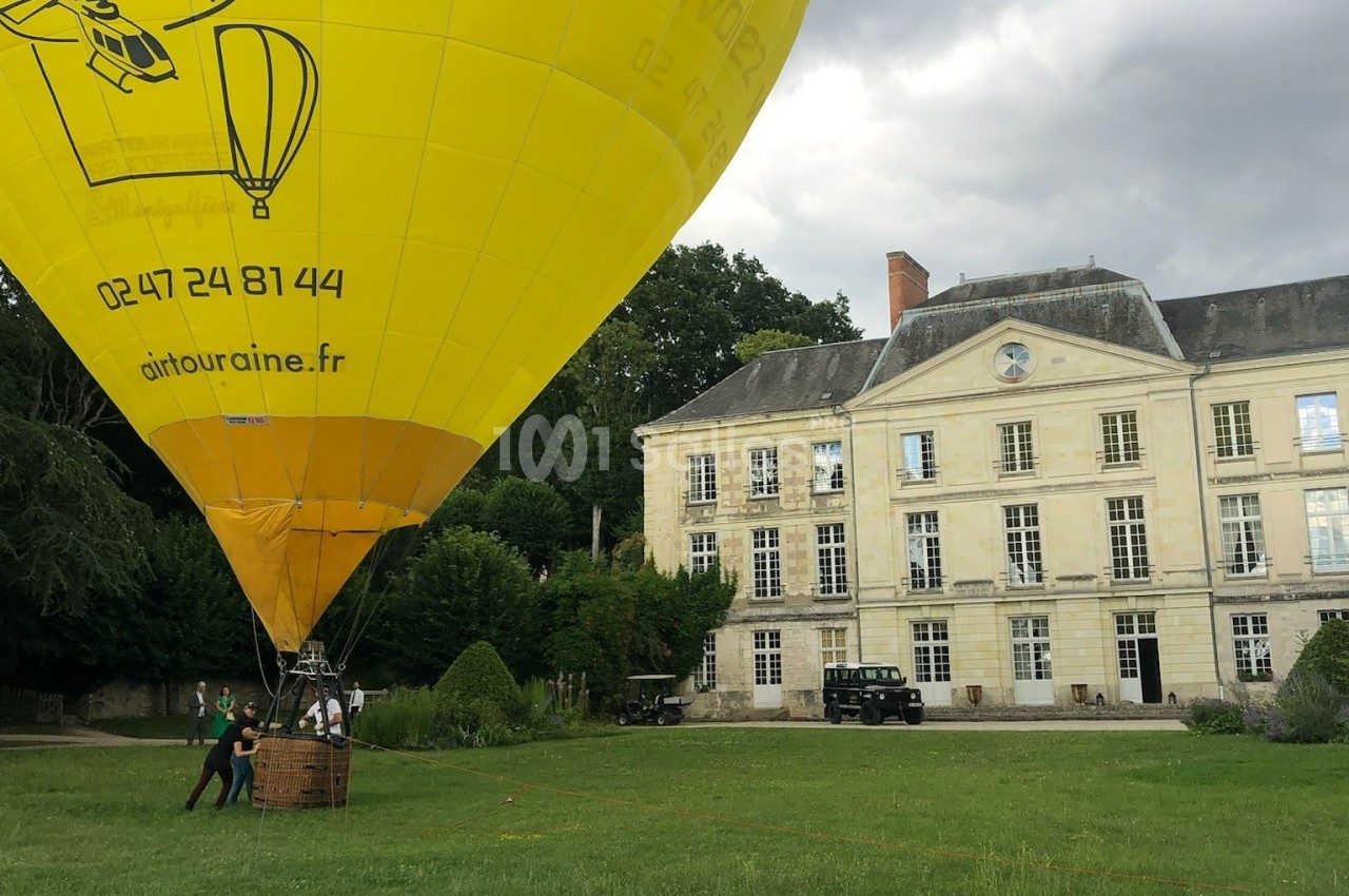 Montgolfière jaune en préparation pour un vol devant un bâtiment historique entouré de verdure.