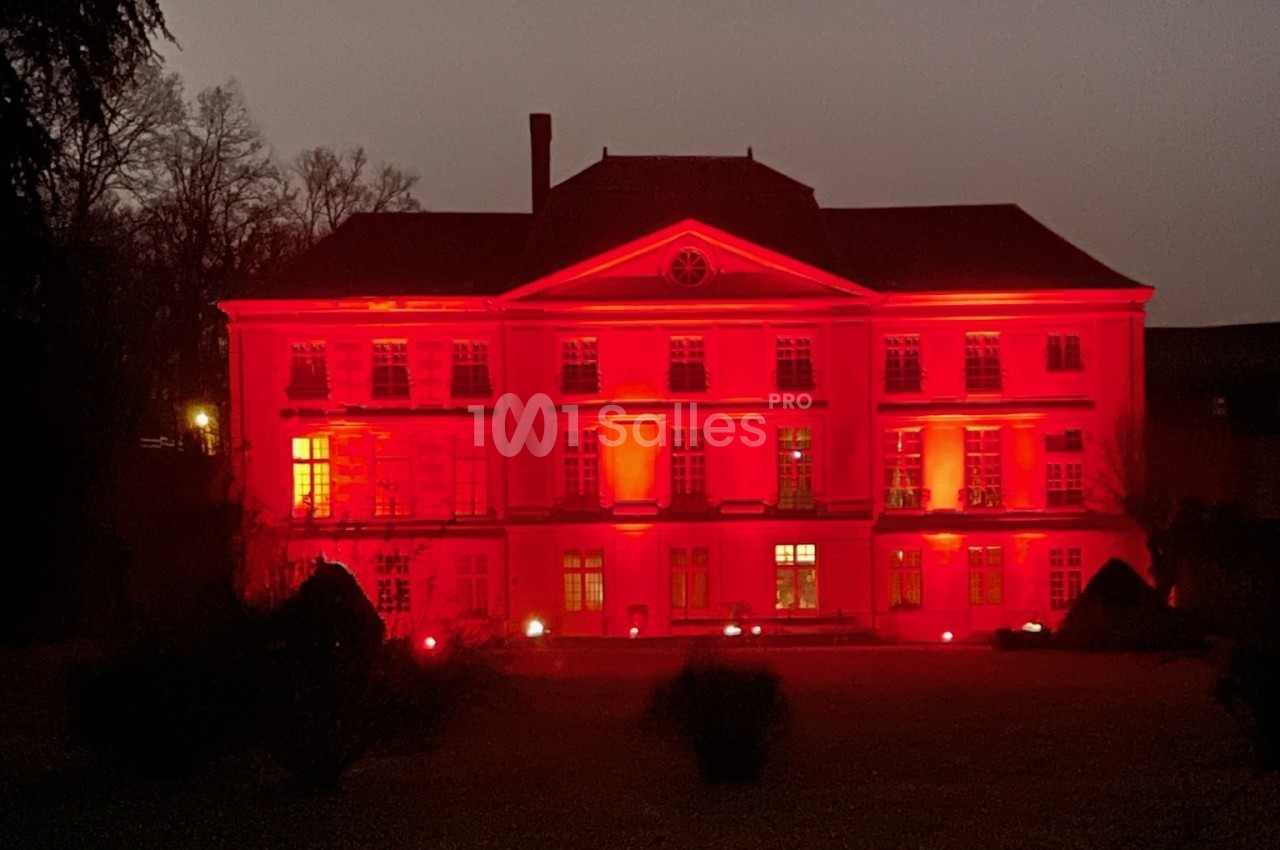 Façade d'un grand bâtiment illuminé en rouge dans un environnement nocturne.