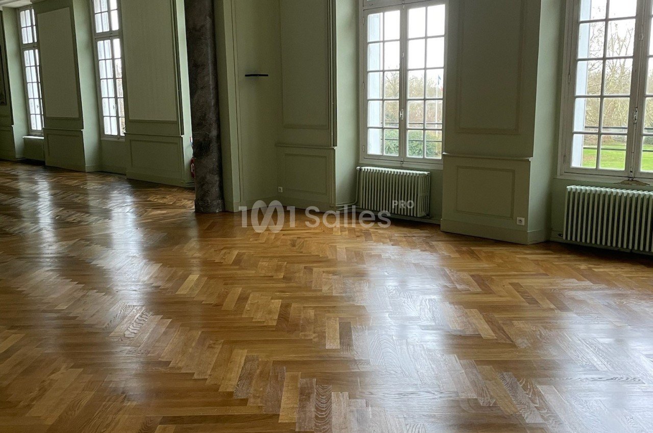 Salle lumineuse avec parquet en chevrons, grandes fenêtres donnant sur un extérieur verdoyant.