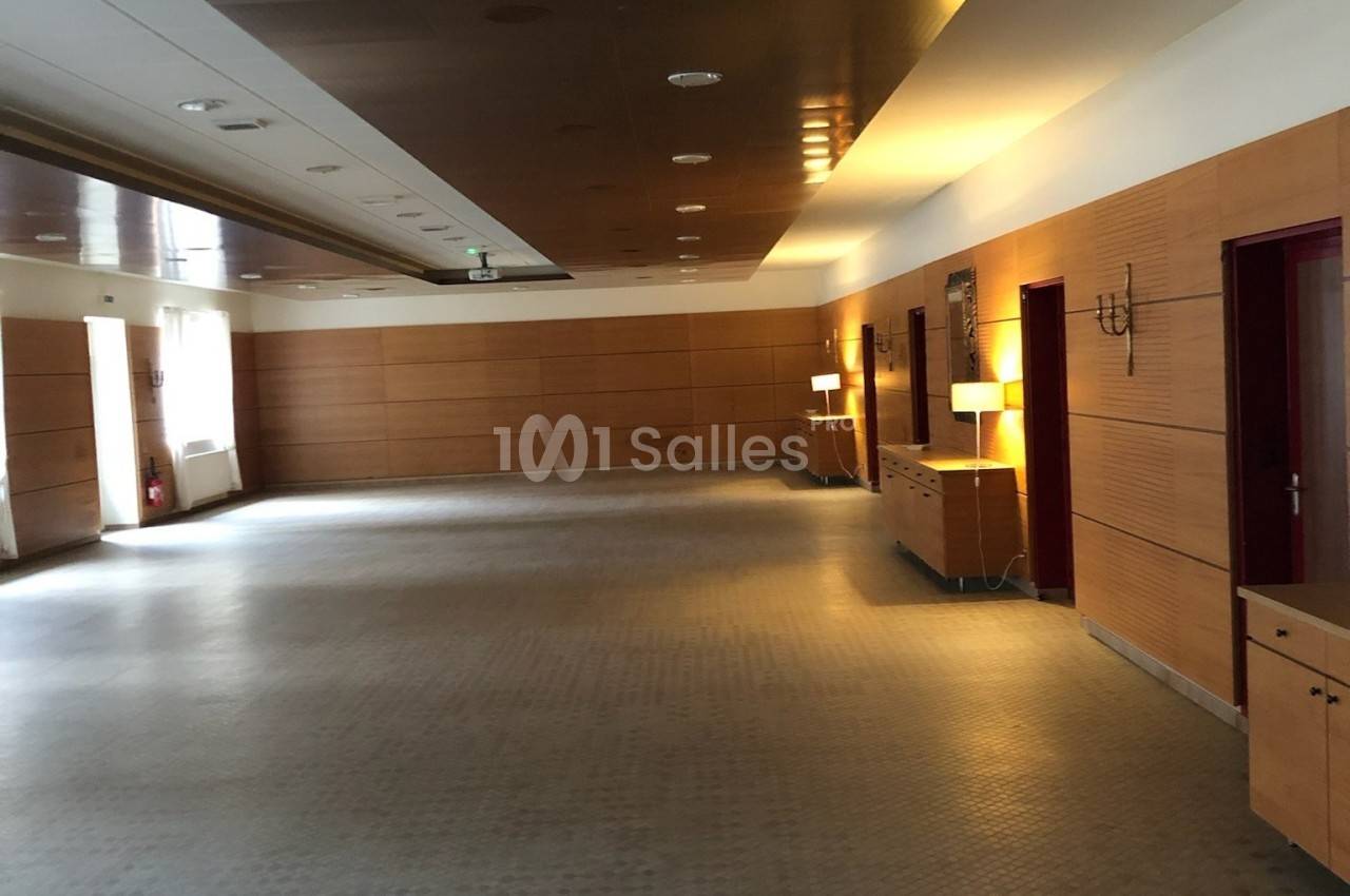 Salle vide avec murs en bois, sol carrelé, éclairage doux et meubles le long des murs.