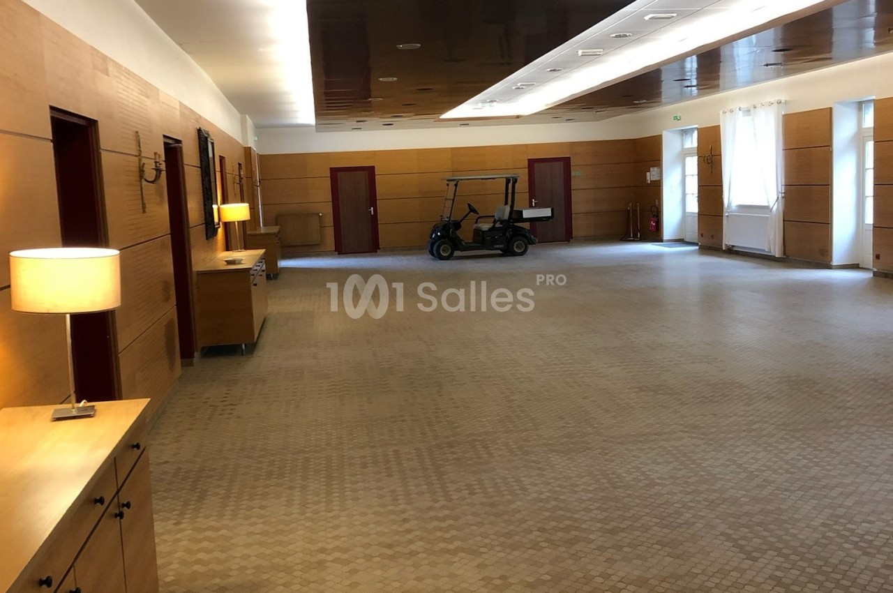 Salle spacieuse avec sol carrelé, murs en bois, lampes allumées et une voiturette stationnée au fond.