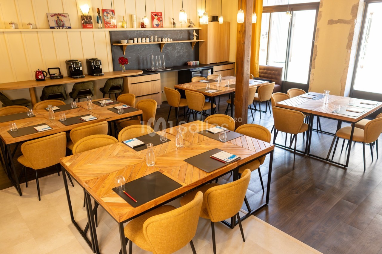 Salle de réunion lumineuse avec tables en bois, chaises jaunes, blocs-notes et carafes d'eau disposés.