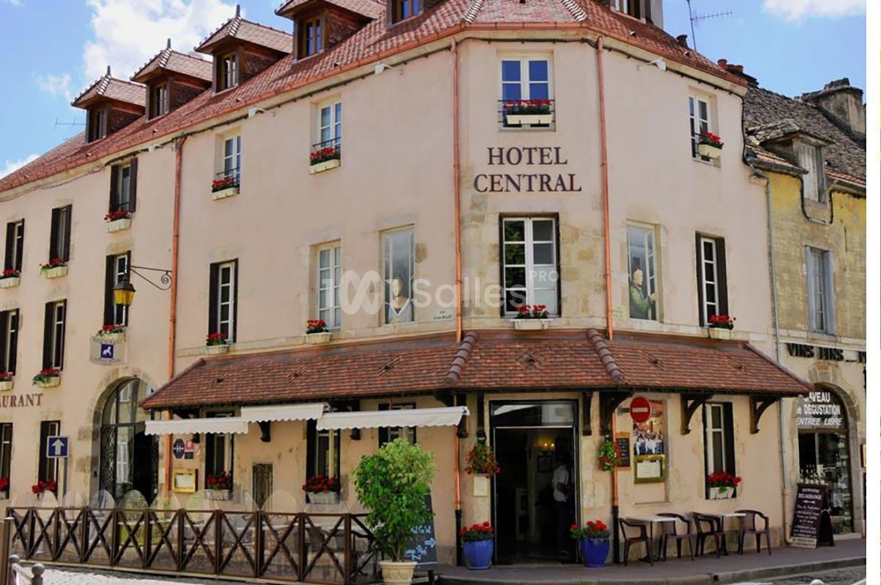 Façade d'un hôtel de style traditionnel avec des volets blancs, des fleurs aux fenêtres et une terrasse extérieure.
