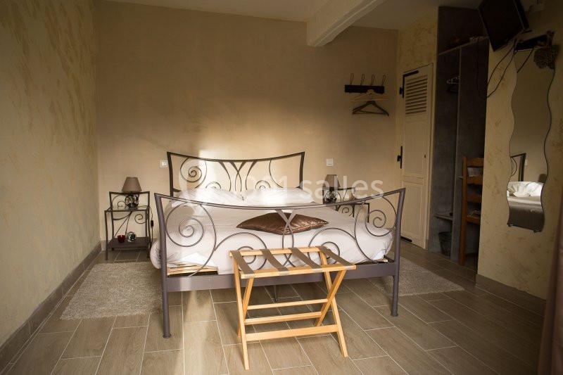 Chambre avec lit double en métal, tables de chevet, miroir, penderie ouverte et sol en carrelage beige.