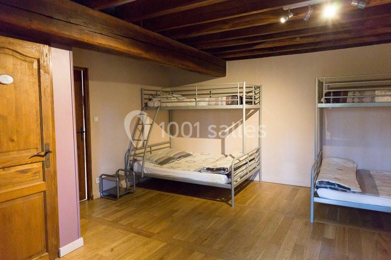 Chambre avec lits superposés en métal, parquet au sol, poutres apparentes au plafond et porte en bois.