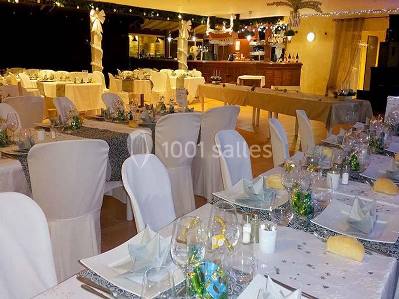 Salle de réception décorée avec des tables dressées pour un repas, ornées de nappes blanches et de décorations festives.