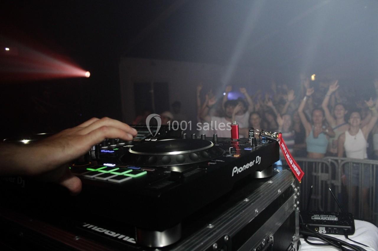 Un DJ mixe sur une console dans une ambiance festive, avec un public dansant en arrière-plan.