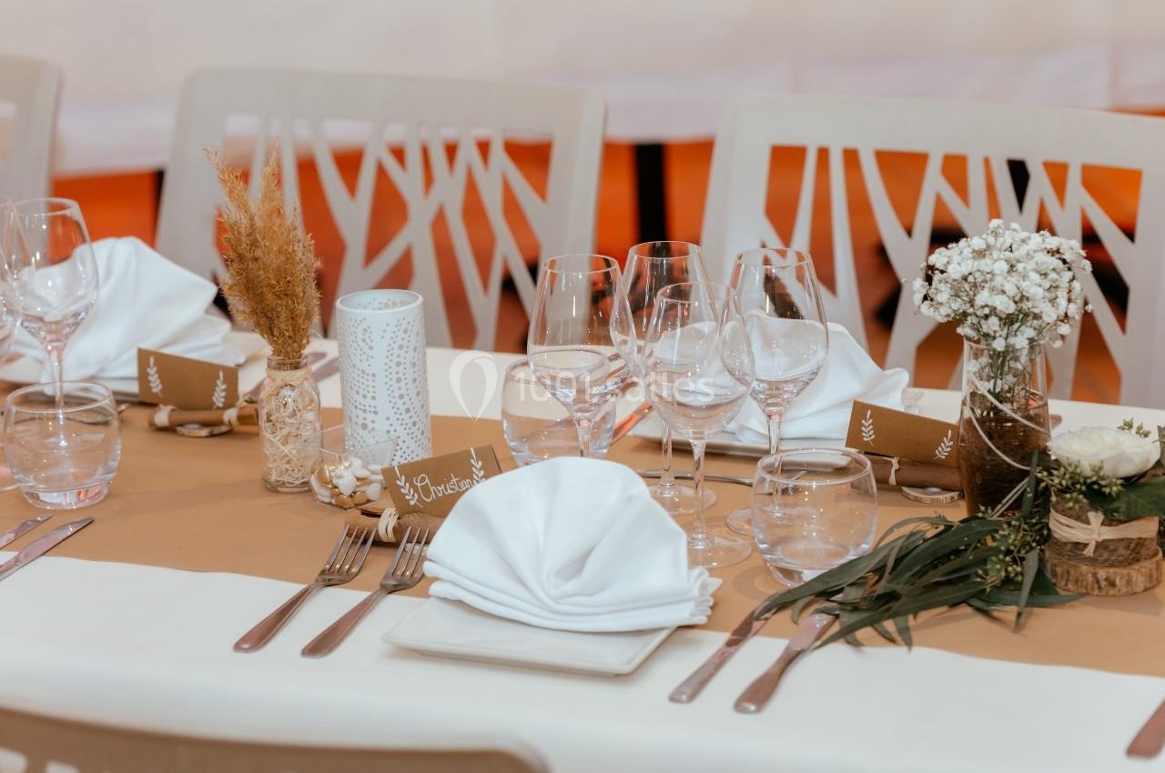 Table dressée avec nappes blanches, serviettes pliées, verres, couverts, et décorations florales naturelles.