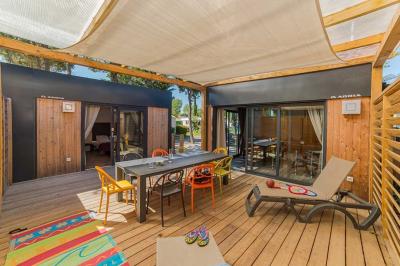 Miniature Location salle Le Barcarès (Pyrénées-Orientales) - Nai'a Village #21 Terrasse en bois avec pergola, mobilier de jardin et façade vitrée donnant sur un espace intérieur moderne.