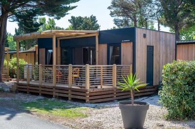 Miniature Location salle Le Barcarès (Pyrénées-Orientales) - Nai'a Village #22 Terrasse en bois avec pergola, mobilier de jardin et façade vitrée donnant sur un espace intérieur moderne.