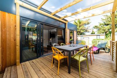 Miniature Location salle Le Barcarès (Pyrénées-Orientales) - Nai'a Village #19 Terrasse en bois avec pergola, mobilier de jardin et façade vitrée donnant sur un espace intérieur moderne.