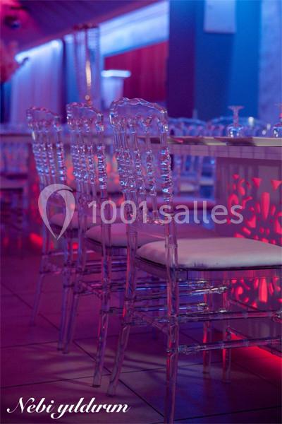 Chaises transparentes alignées autour d'une table dans une salle éclairée par des lumières colorées.
