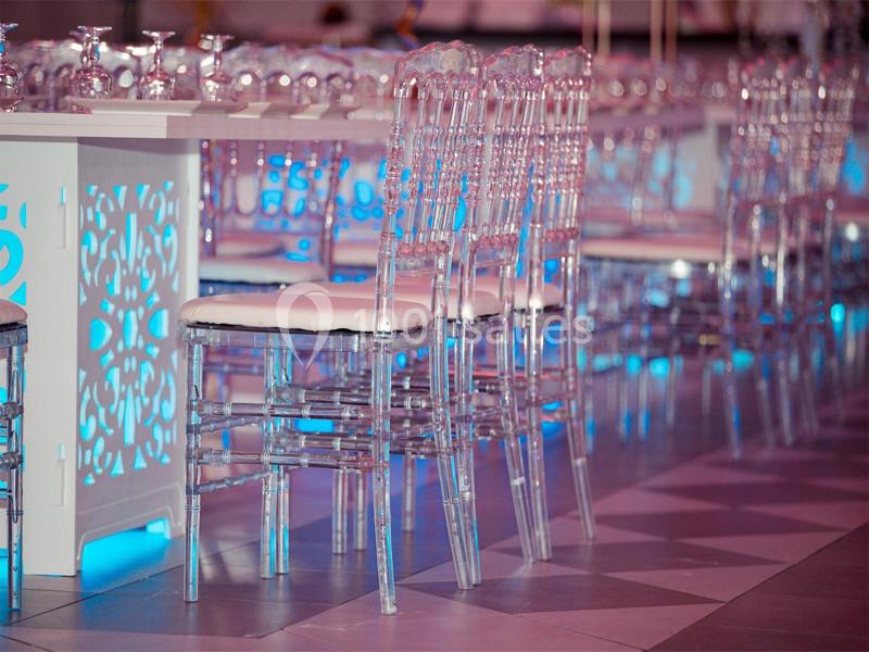 Chaises transparentes alignées autour d'une table blanche décorée, éclairage bleu en arrière-plan.