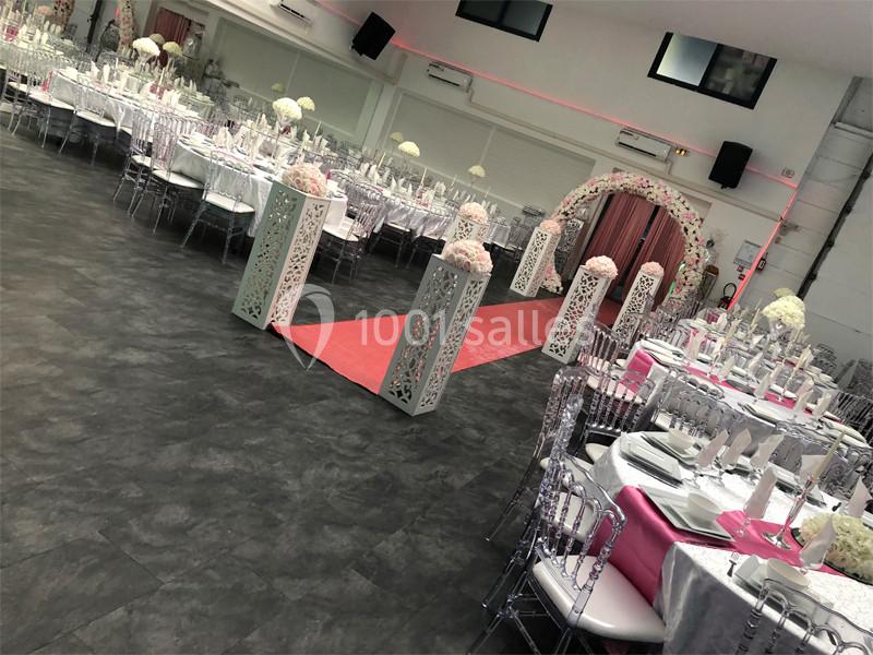 Salle de réception décorée avec des tables dressées, un tapis rouge et une arche fleurie pour un événement festif.