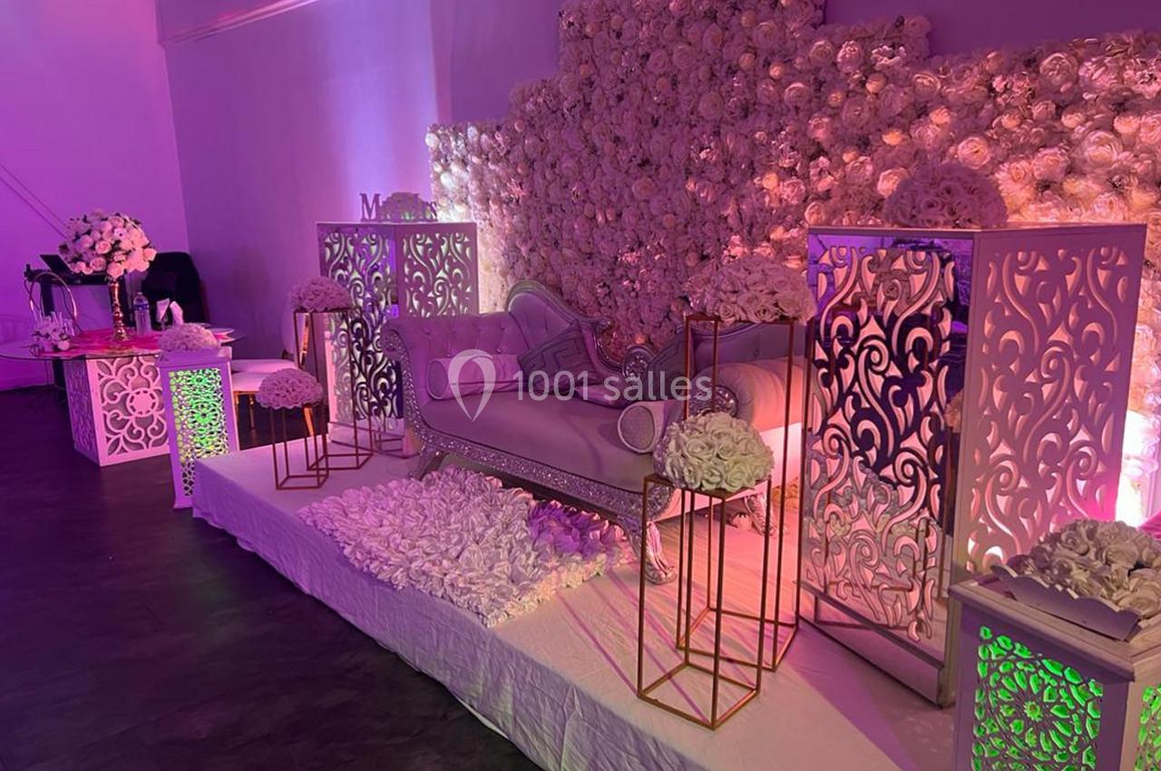 Décor de mariage avec canapé, murs ornés de fleurs blanches et éclairage rose dans une ambiance élégante.