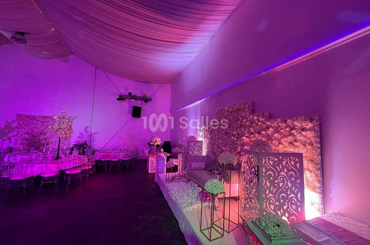 Salle de réception décorée avec des fleurs, des tables dressées et un éclairage violet tamisé.