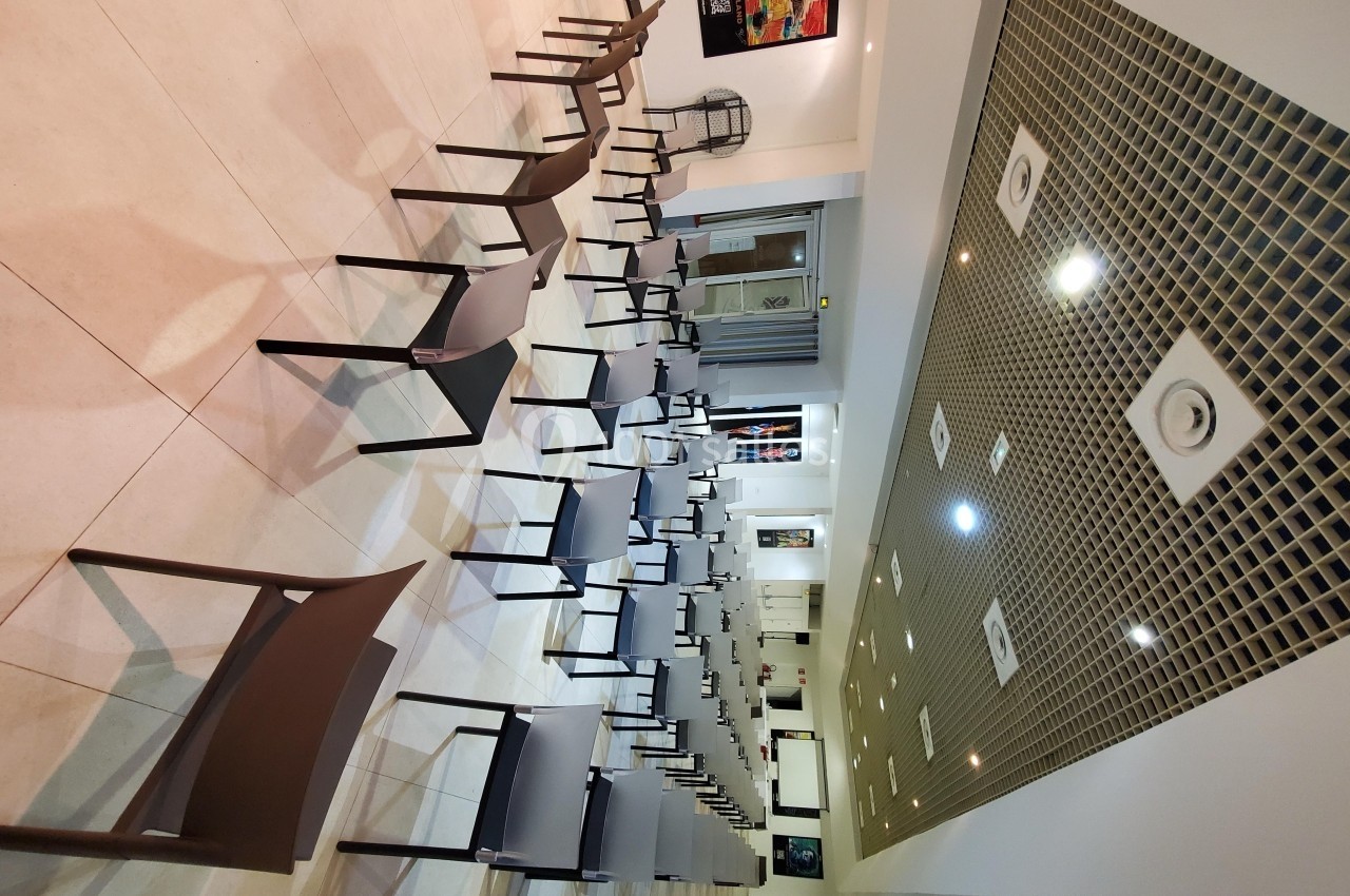 Salle de conférence moderne avec des rangées de chaises vides alignées sous un plafond à panneaux géométriques.