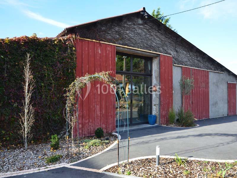 Façade d'un bâtiment avec murs en bardage rouge, entrée vitrée et allée bordée de végétation.