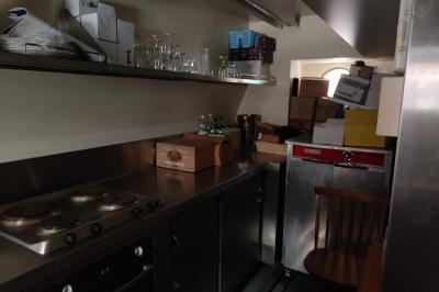 Miniature Location salle Suresnes (Hauts-de-Seine) - La Petite Péniche du 92 #6 Cuisine étroite avec plaques de cuisson, étagères remplies de cartons et vaisselle, et un réfrigérateur en acier inoxydable.