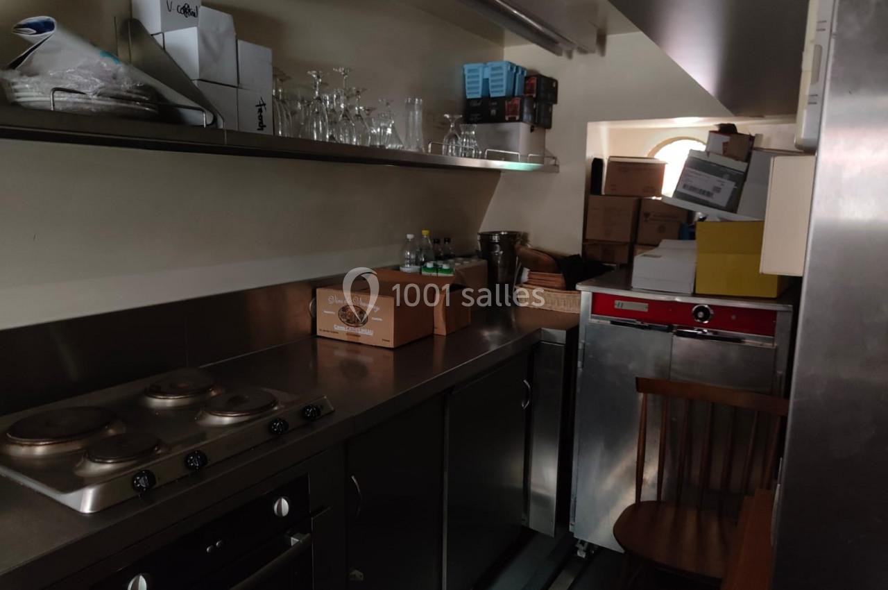 Cuisine étroite avec plaques de cuisson, étagères remplies de cartons et vaisselle, et un réfrigérateur en acier inoxydable.