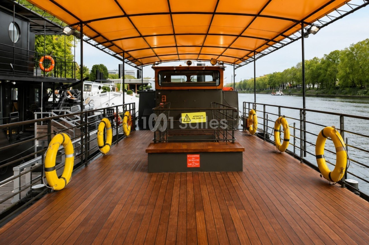 Pont en bois d'un bateau avec toit orange, bouées de sauvetage jaunes et vue sur une rivière bordée d'arbres.