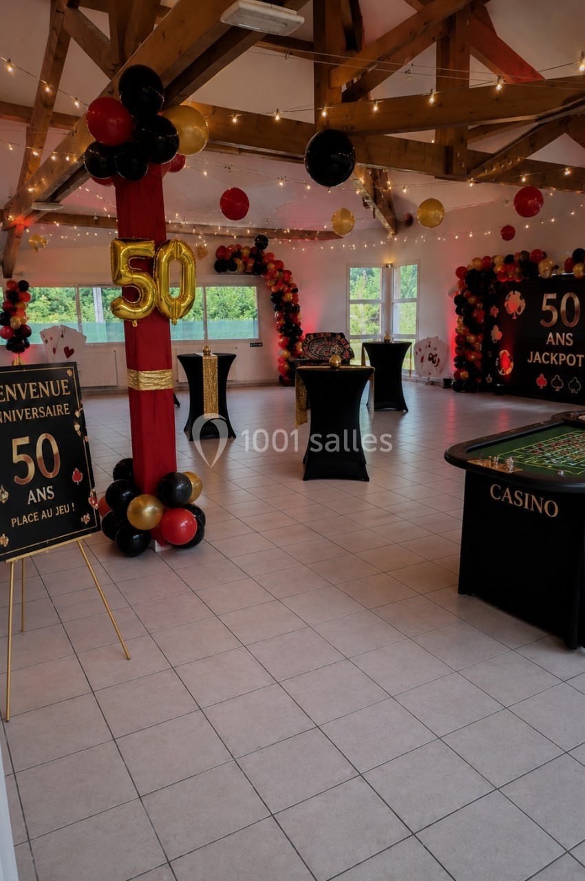 Salle décorée sur le thème du casino pour un 50e anniversaire, avec ballons, tables de jeu et panneaux festifs.
