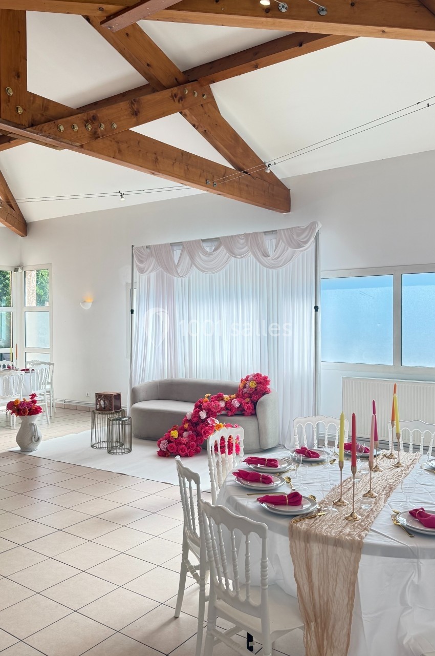 Salle lumineuse avec poutres apparentes, table décorée pour un événement et canapé orné de fleurs roses.