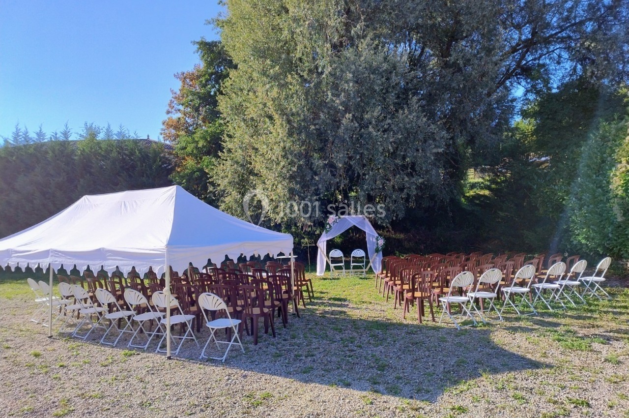 Chaises disposées sous une tente blanche et en plein air, face à une arche décorative pour une cérémonie en extérieur.