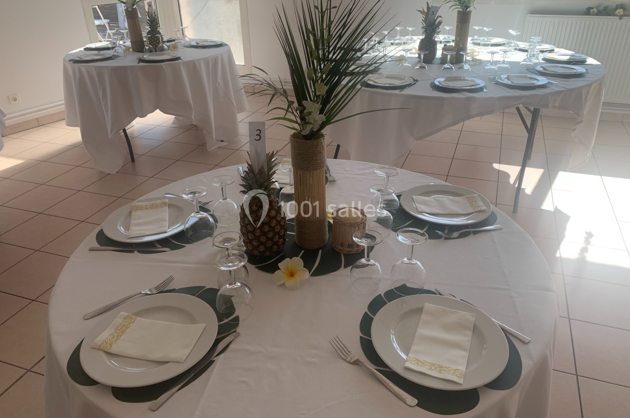 Table dressée avec une décoration tropicale, comprenant des ananas, des feuilles et des fleurs, dans une salle lumineuse.