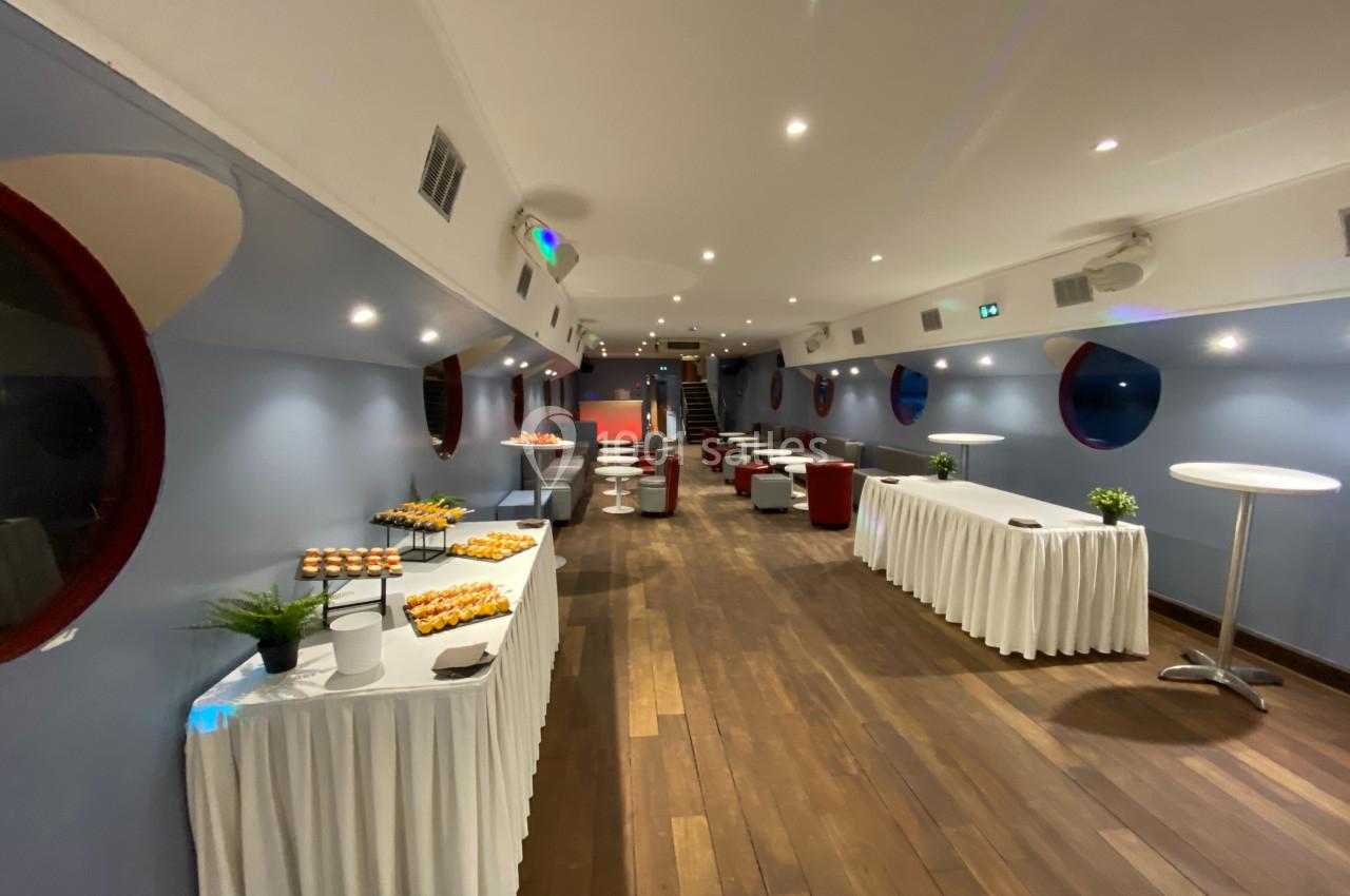 Salle aménagée avec des tables dressées pour un buffet, décor moderne avec murs bleus et hublots rouges.