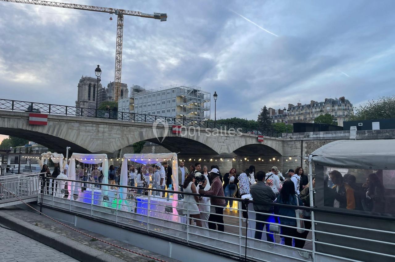 Groupe de personnes rassemblées sur un quai près d'un pont, avec des décorations lumineuses et une grue en arrière-plan.