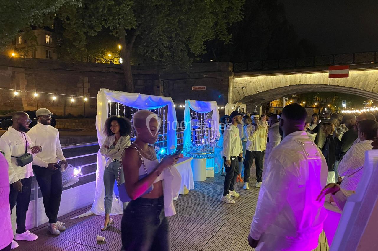 Des personnes en tenue blanche et décontractée discutent et se détendent lors d'un événement nocturne en plein air près d'un…