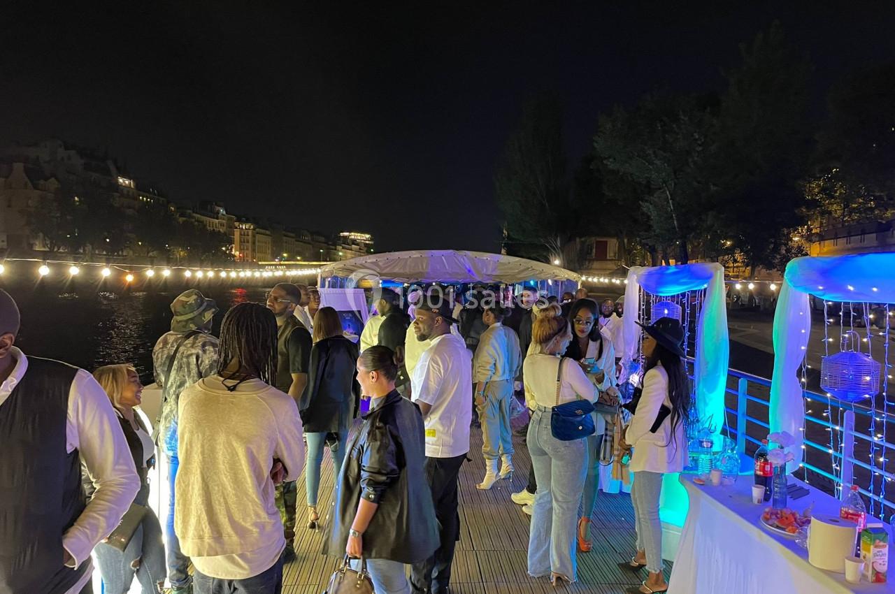 Groupe de personnes socialisant sur une péniche éclairée, décorée de guirlandes lumineuses, en soirée.