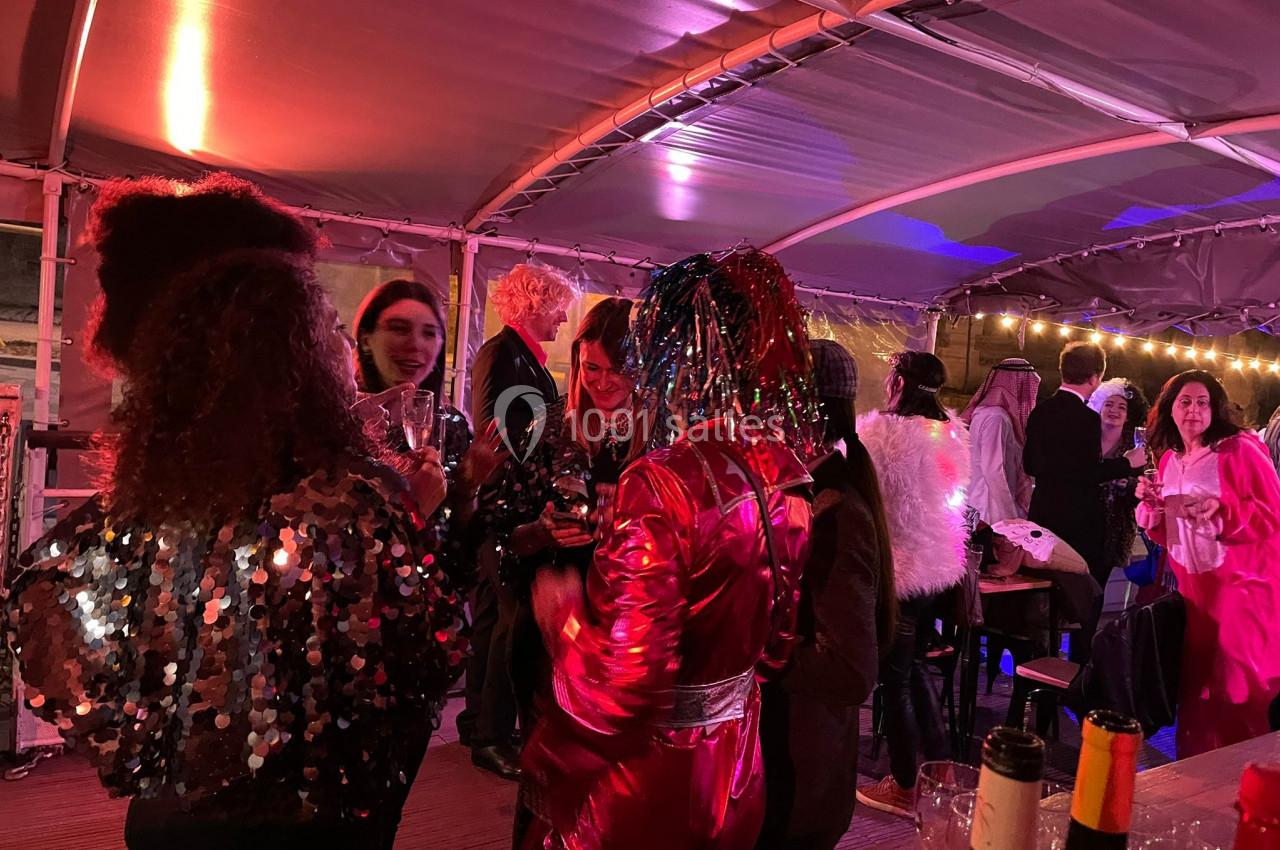 Personnes en costumes festifs discutant et partageant un moment convivial sous un chapiteau éclairé.