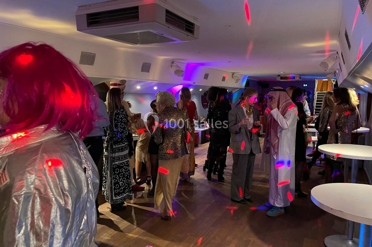 Personnes en tenue festive discutant et dansant dans une salle éclairée par des lumières colorées.