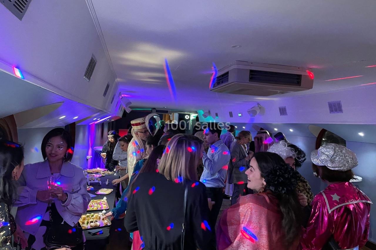 Groupe de personnes discutant et partageant un buffet dans une salle éclairée par des lumières colorées.