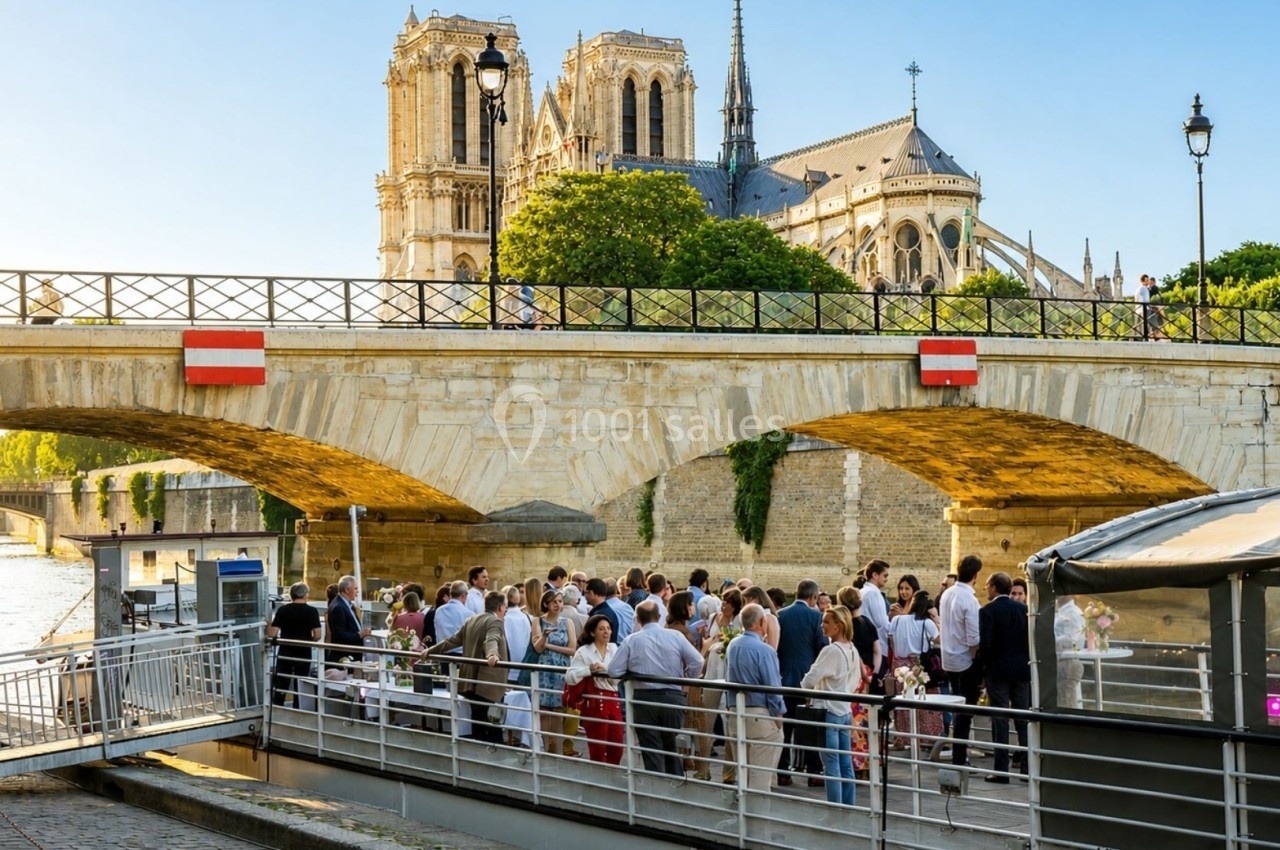 Groupe de personnes rassemblées sur un quai près d'un pont, avec la cathédrale Notre-Dame en arrière-plan.