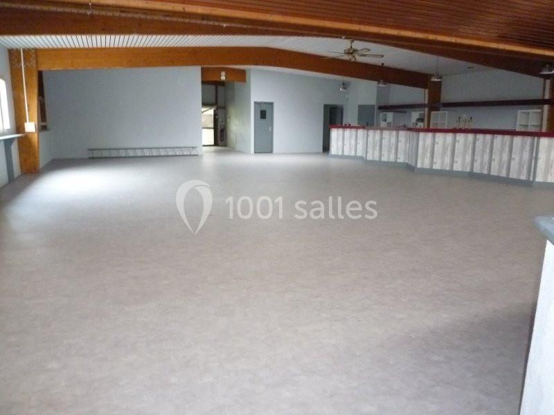 Salle spacieuse avec sol clair, plafond en bois et comptoir long, éclairée par des fenêtres latérales.