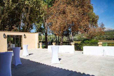 Façade d'une maison méditerranéenne avec terrasse, jardin aménagé et statues, entourée d'arbres sous un ciel dégagé.