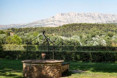 Façade d'une maison méditerranéenne avec terrasse, jardin aménagé et statues, entourée d'arbres sous un ciel dégagé.