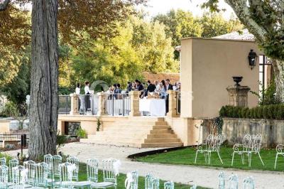 Façade d'une maison méditerranéenne avec terrasse, jardin aménagé et statues, entourée d'arbres sous un ciel dégagé.