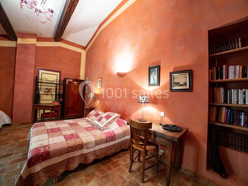 Chambre avec murs orangés, lit double à motifs, bureau en bois, étagères remplies de livres et sol en carrelage.
