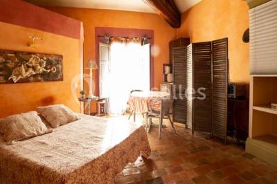 Façade d'une maison méditerranéenne avec terrasse, jardin aménagé et statues, entourée d'arbres sous un ciel dégagé.