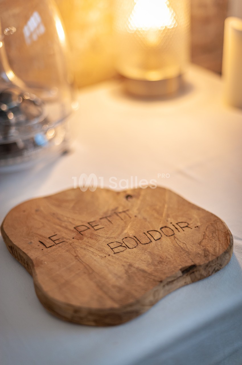 Planche en bois gravée ’Le Petit Boudoir’ posée sur une table éclairée par une lumière douce.