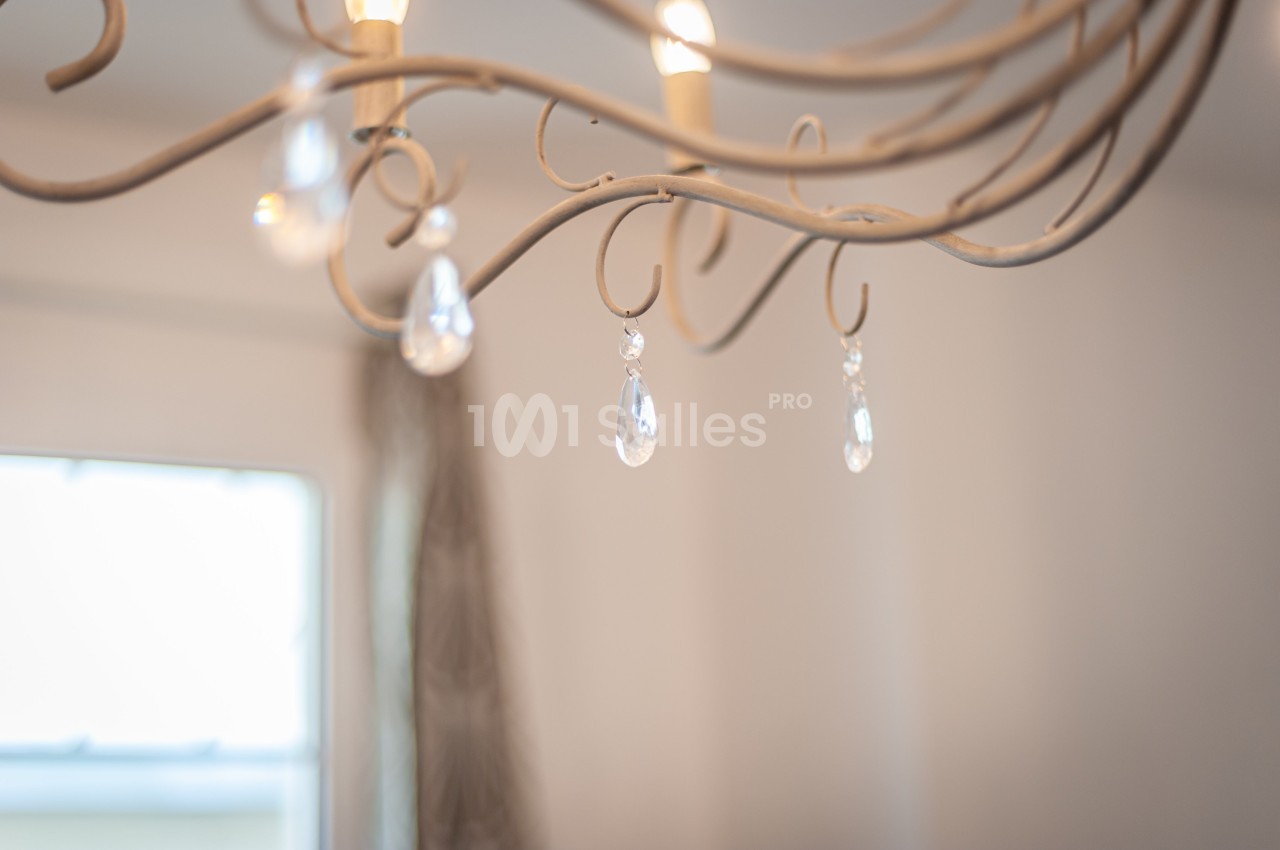 Lustre en métal avec pampilles en verre suspendues, éclairé dans une pièce lumineuse avec un fond flou.