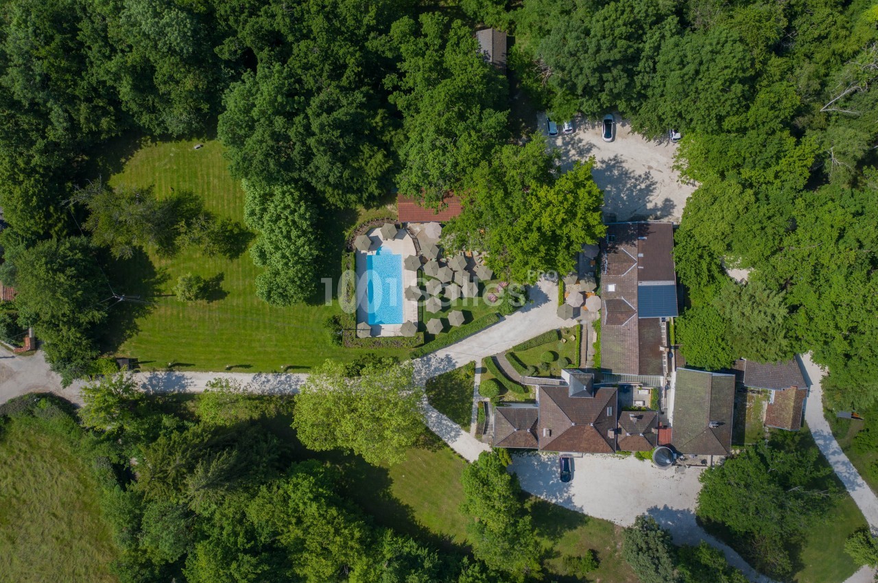 Vue aérienne d'une propriété entourée de verdure avec piscine, terrasses et bâtiments en pierre.