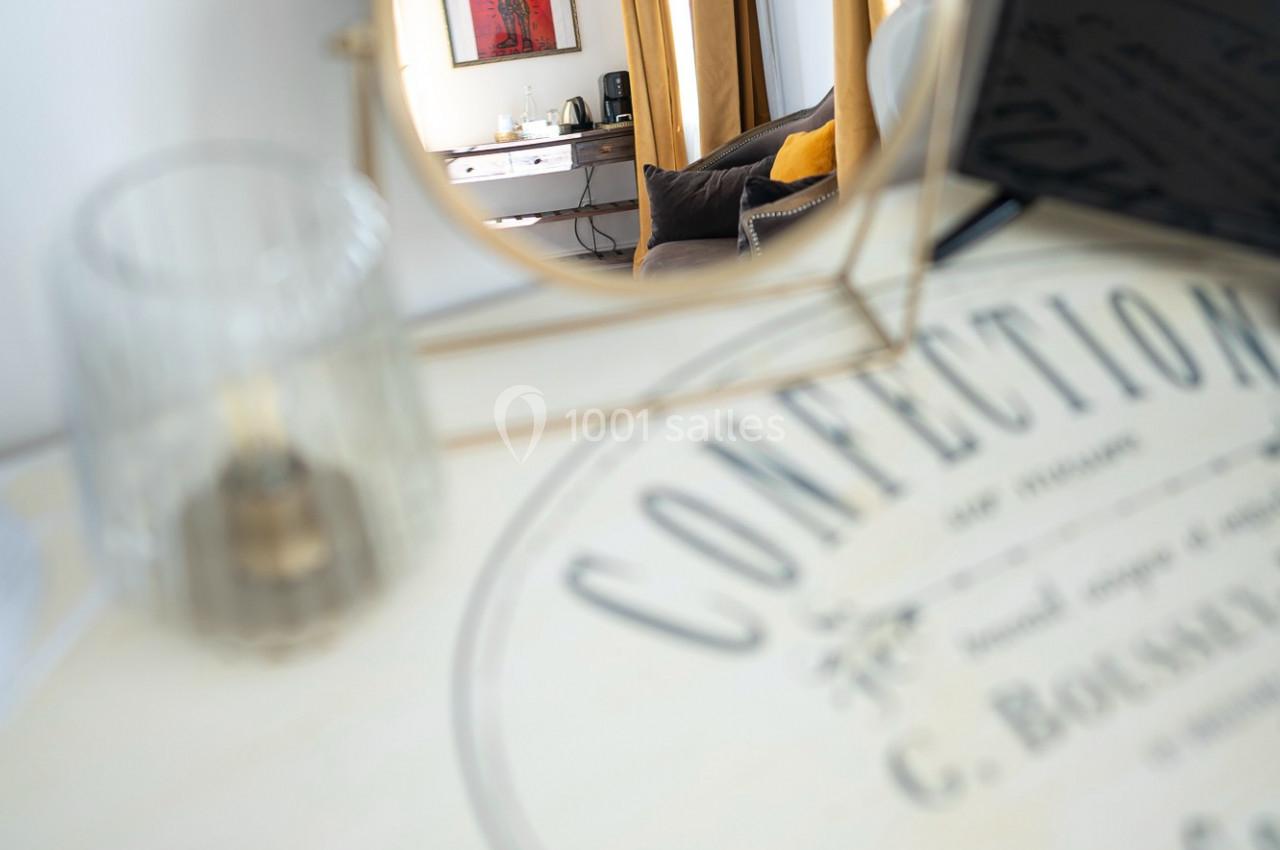Un miroir rond reflète un intérieur lumineux avec des rideaux dorés, un canapé et un tableau rouge au mur.