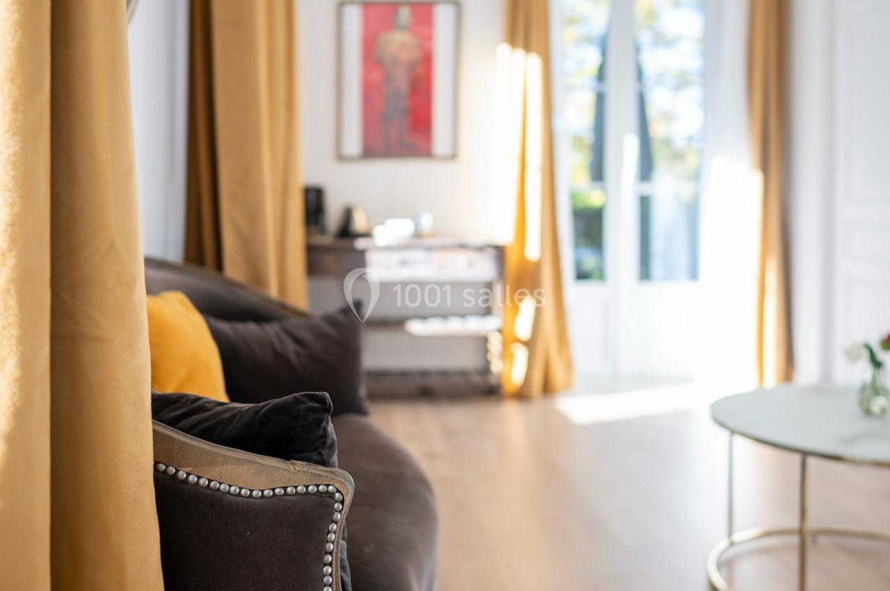 Salon lumineux avec canapé sombre, rideaux jaunes, table basse ronde et grande fenêtre donnant sur l'extérieur.