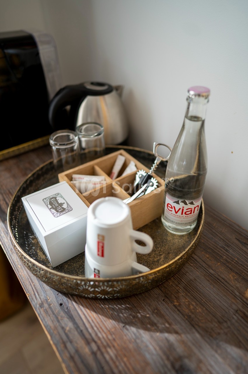 Plateau avec une bouteille d'eau, tasses empilées, sachets de thé, cuillères et une bouilloire en arrière-plan.